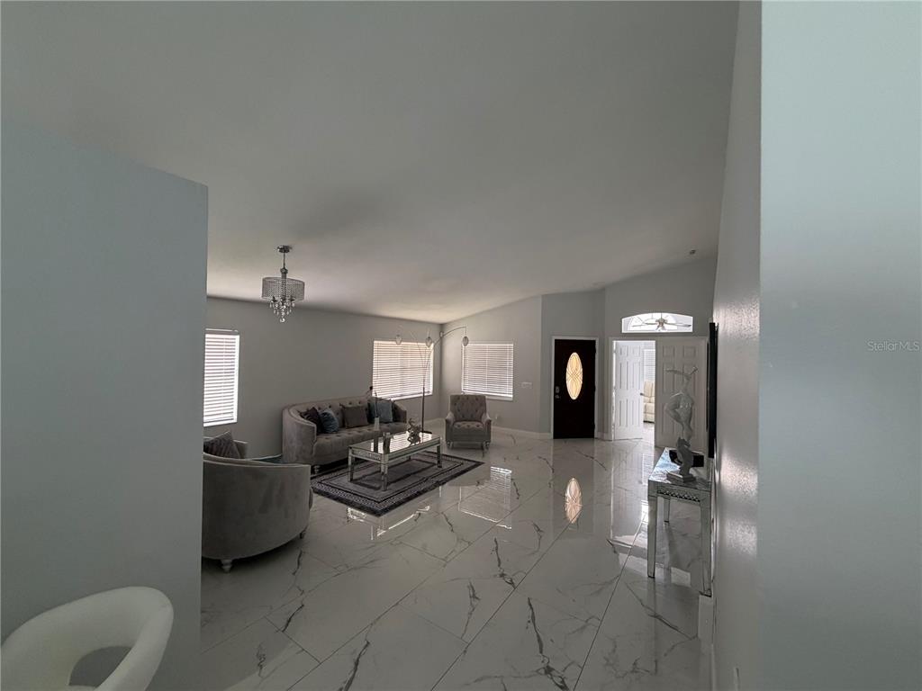 A living room features white marble-look tile flooring, a grey sofa, and a crystal chandelier — 3264 FAIRFIELD DRIVE, KISSIMMEE, FL