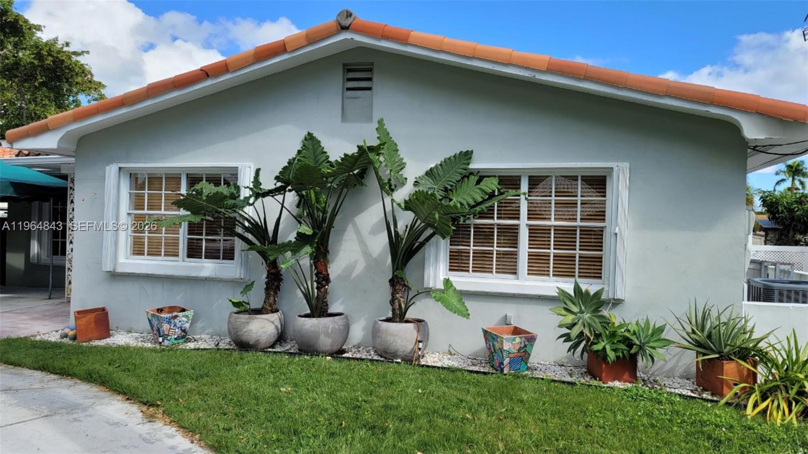 The exterior of a light-colored house features large potted plants and two windows — 12945 Cherry Rd, North Miami FL 33181, NORTH MIAMI, FL