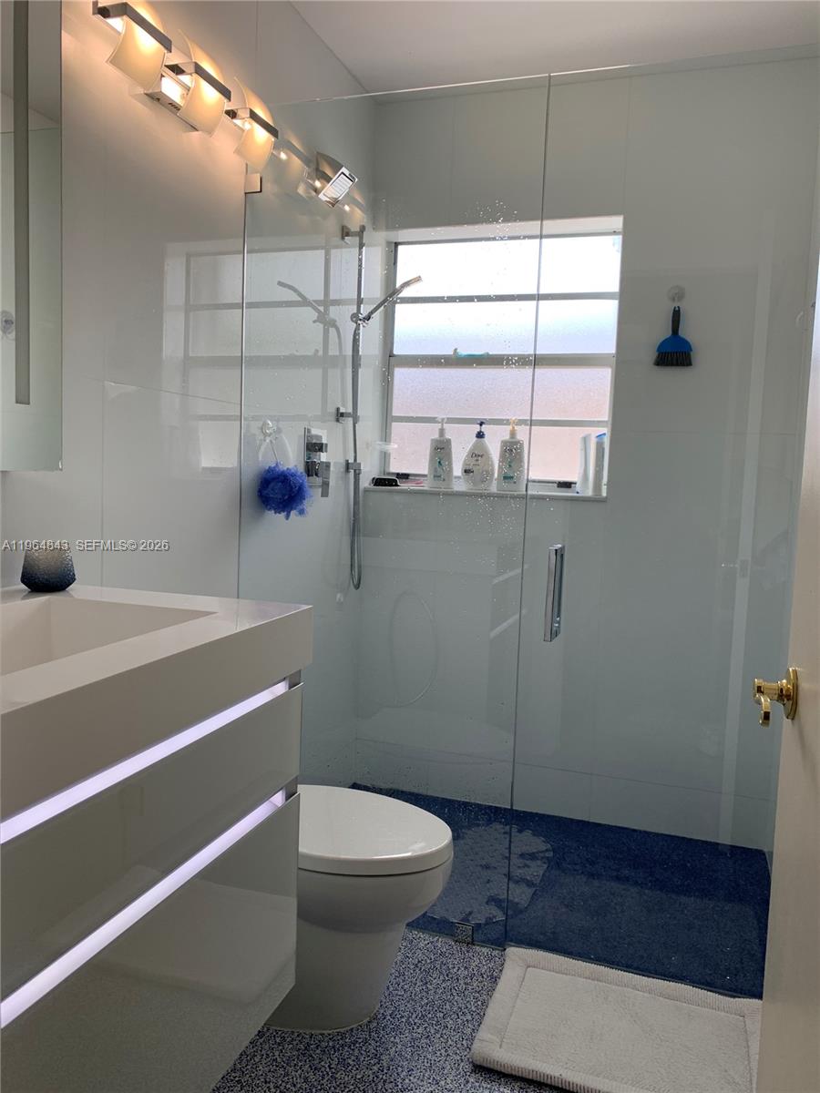 A modern bathroom features a glass-enclosed shower, a floating vanity, and blue speckled flooring — 12945 Cherry Rd, North Miami FL 33181, NORTH MIAMI, FL