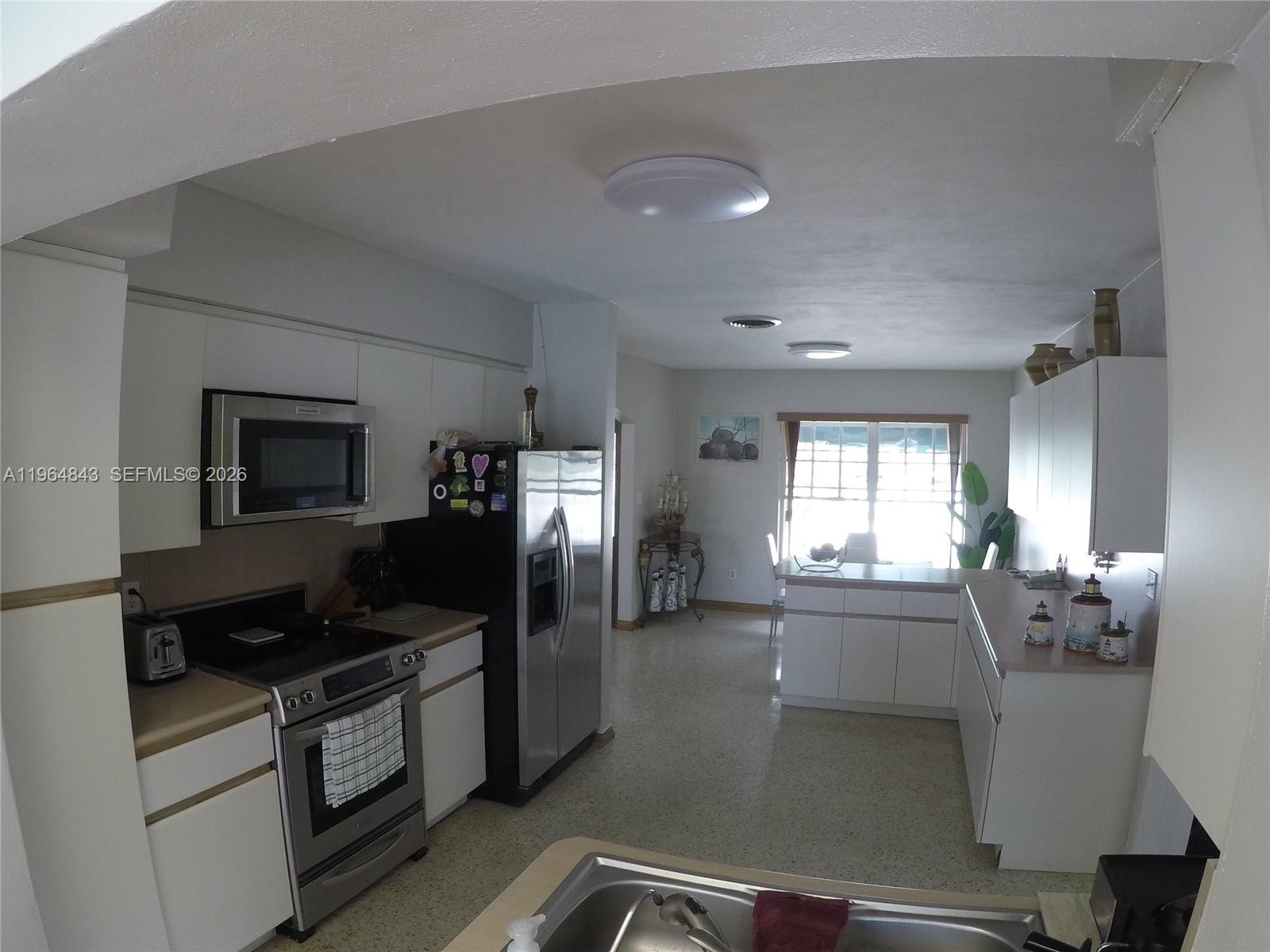 A kitchen features white cabinetry, stainless steel appliances, and a light-colored speckled floor — 12945 Cherry Rd, North Miami FL 33181, NORTH MIAMI, FL
