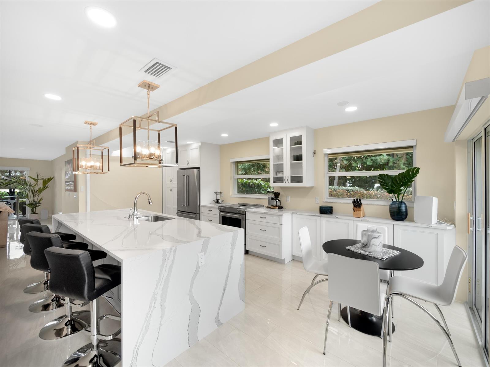 A modern kitchen features a large marble-topped island, white cabinetry, and a small dining area — 4161 S Us Highway 1 # N1, Jupiter FL 33477, JUPITER, FL