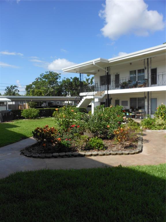 A two-story apartment building features a landscaped garden bed and a covered parking area — 138 36TH AVENUE N UNIT 206W, ST PETERSBURG, FL