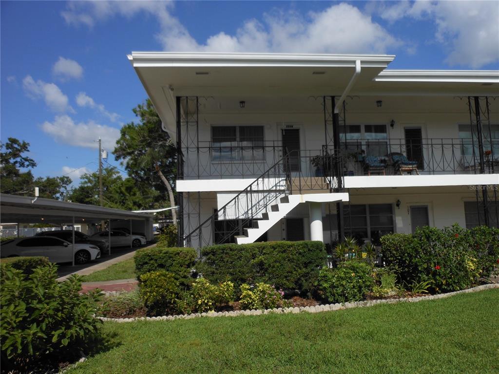 A two-story apartment building features an exterior staircase, a covered parking area, and landscaping — 138 36TH AVENUE N UNIT 206W, ST PETERSBURG, FL
