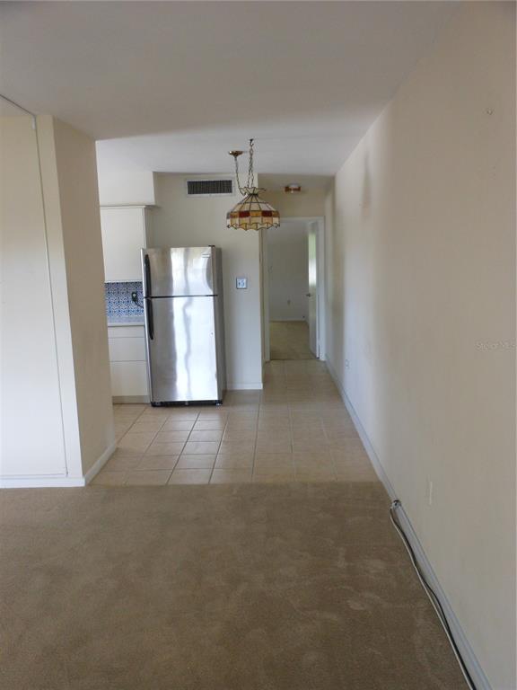 A view from a carpeted room into a tiled kitchen area with a stainless refrigerator — 138 36TH AVENUE N UNIT 206W, ST PETERSBURG, FL