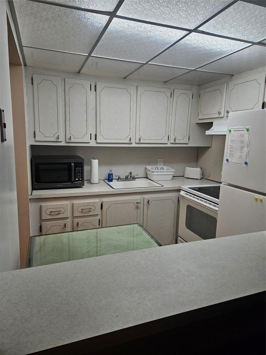 A small kitchen features light wood-grain cabinets, white appliances, and a drop ceiling — 82 Tilford D # 82, Deerfield Beach FL 33442, DEERFIELD BEACH, FL