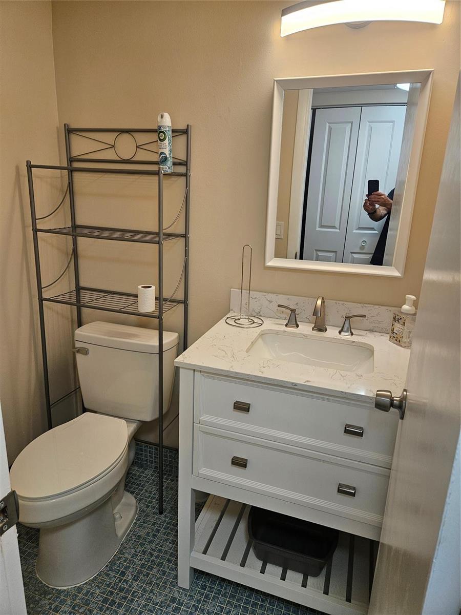 A bathroom features a white vanity with a marble countertop, a toilet, and metal shelving — 82 Tilford D # 82, Deerfield Beach FL 33442, DEERFIELD BEACH, FL