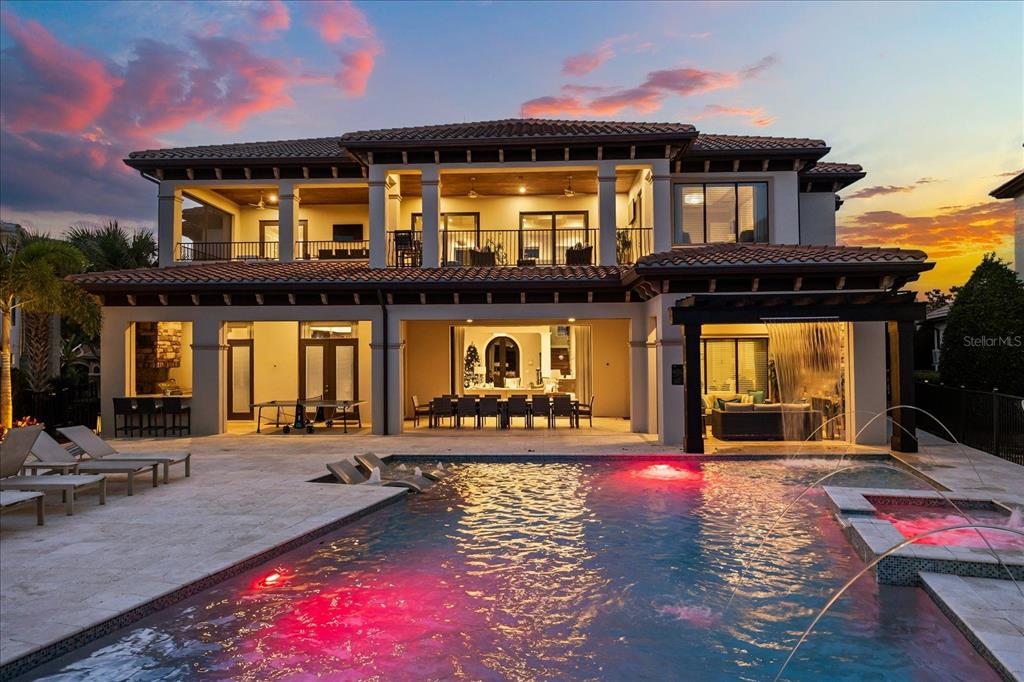A two-story luxury home features a swimming pool, covered patio, and balcony at sunset — 7840 PALMILLA COURT, REUNION, FL