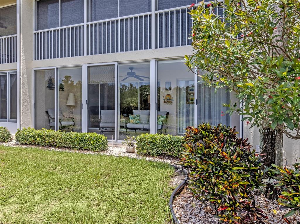 A ground-floor patio with glass sliding doors, outdoor furniture, and a landscaped yard — 210 SILVER LAKE DRIVE UNIT 102, VENICE, FL