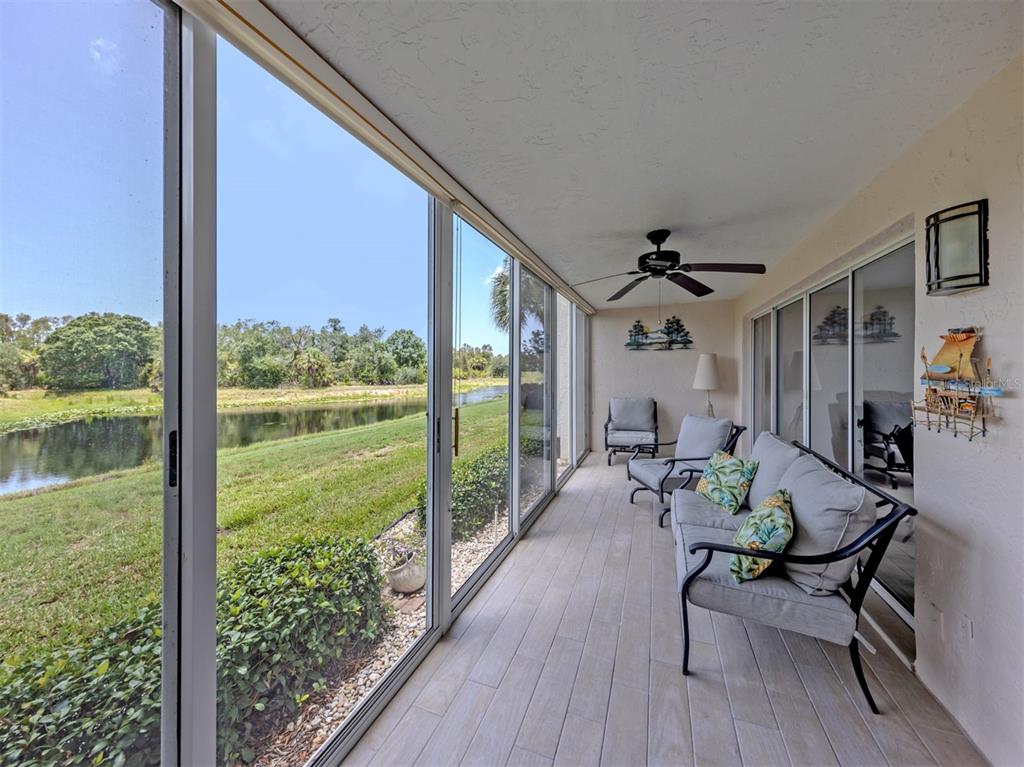 A screened-in porch features light wood-look tile flooring, patio furniture, and a view of a pond — 210 SILVER LAKE DRIVE UNIT 102, VENICE, FL