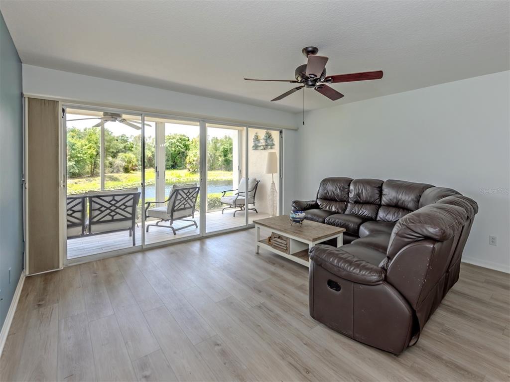 A living room features light wood-look flooring, a brown leather sectional, and sliding glass doors — 210 SILVER LAKE DRIVE UNIT 102, VENICE, FL