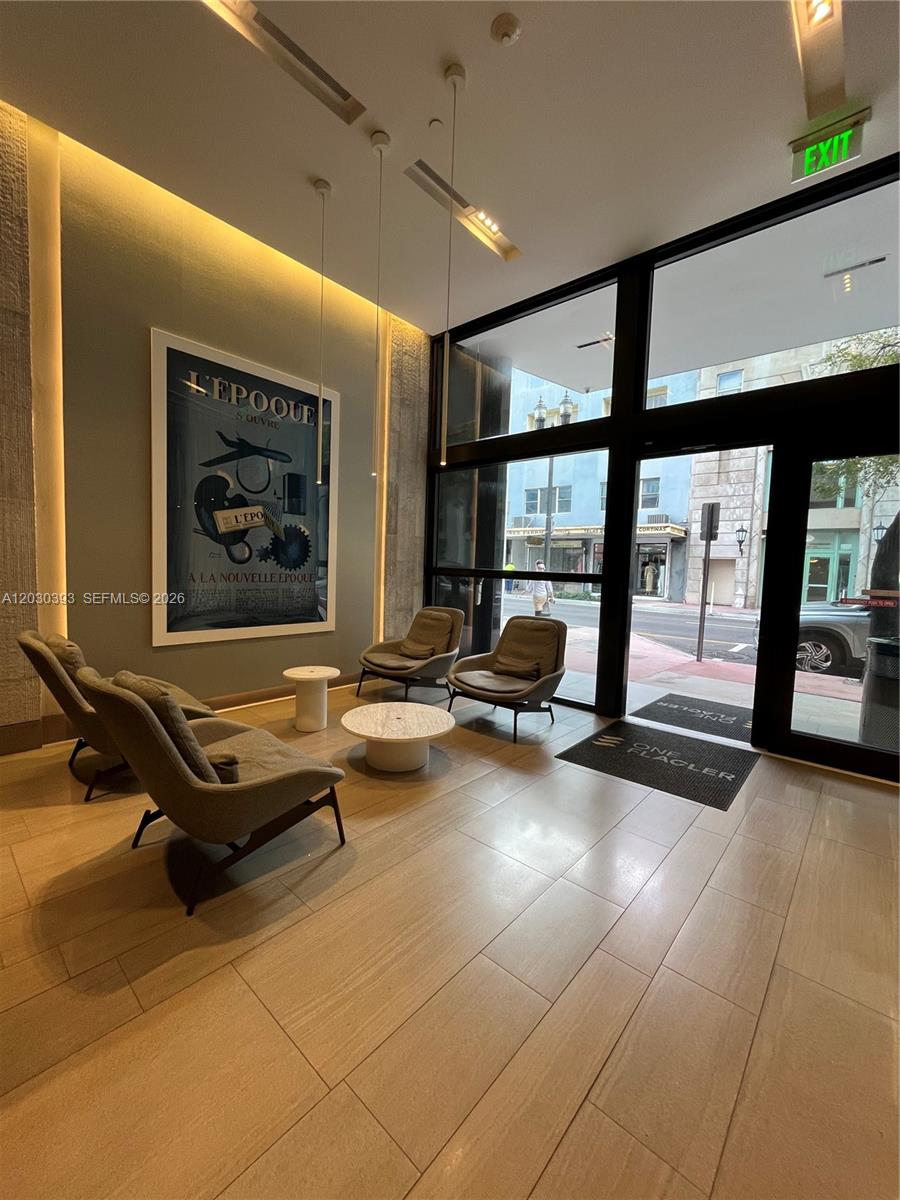 A modern lobby features four gray armchairs, two round tables, and a large framed poster — 14 NE 1st Ave # 1210, Miami FL 33132, MIAMI, FL