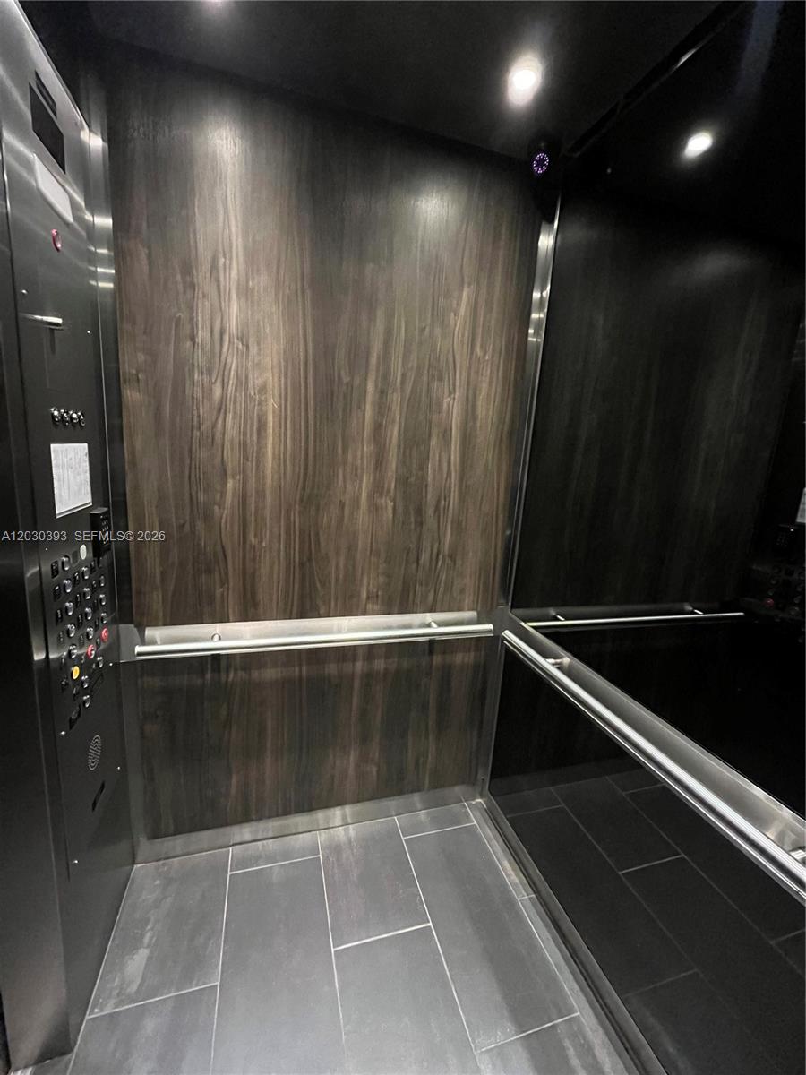 The interior of an elevator features dark wood paneling, stainless steel accents, and tile flooring — 14 NE 1st Ave # 1210, Miami FL 33132, MIAMI, FL
