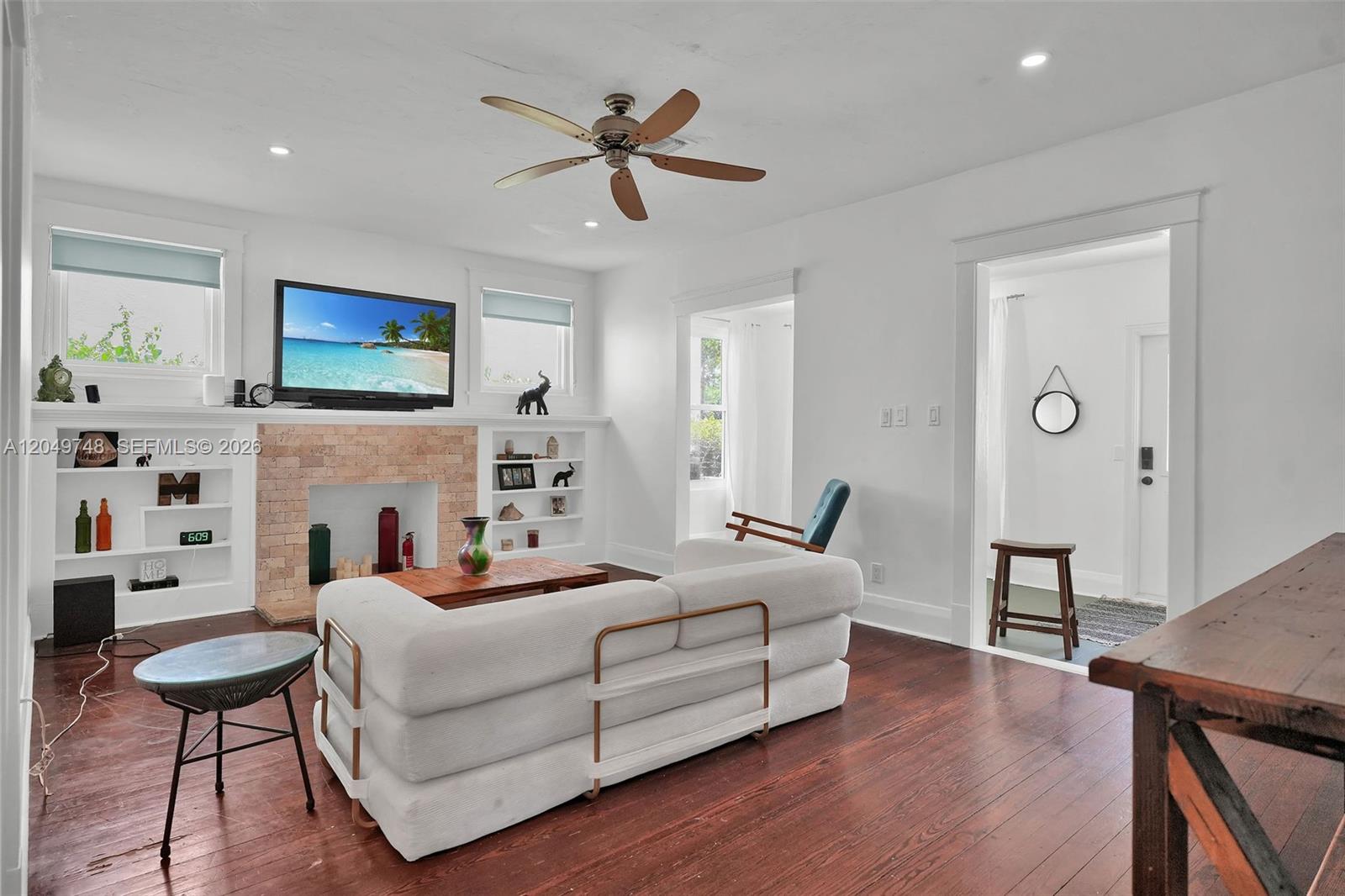 A living room features a brick fireplace, built-in shelving, a white sofa, and hardwood floors — 1933 Madison St, Hollywood FL 33020, HOLLYWOOD, FL