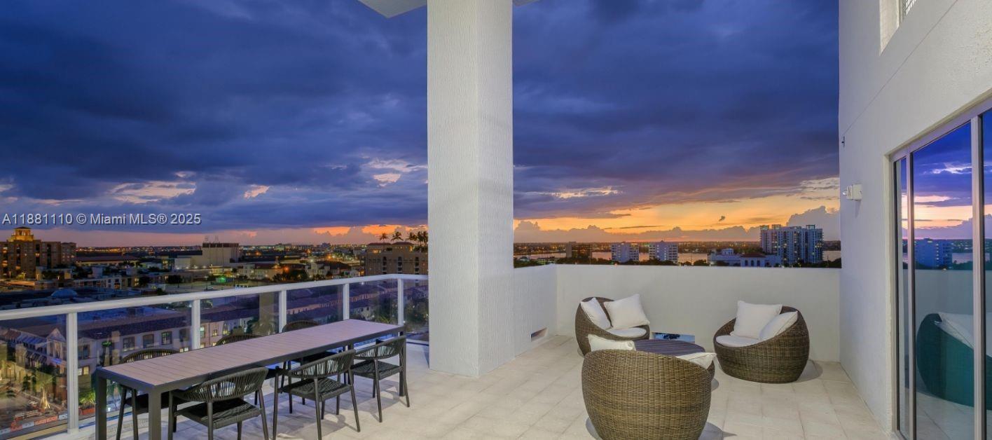 A balcony features a dining table, wicker chairs, and a panoramic view of a city sunset — 591 Evernia  Sreet # A13, West Palm Beach FL 33401, WEST PALM BEACH, FL