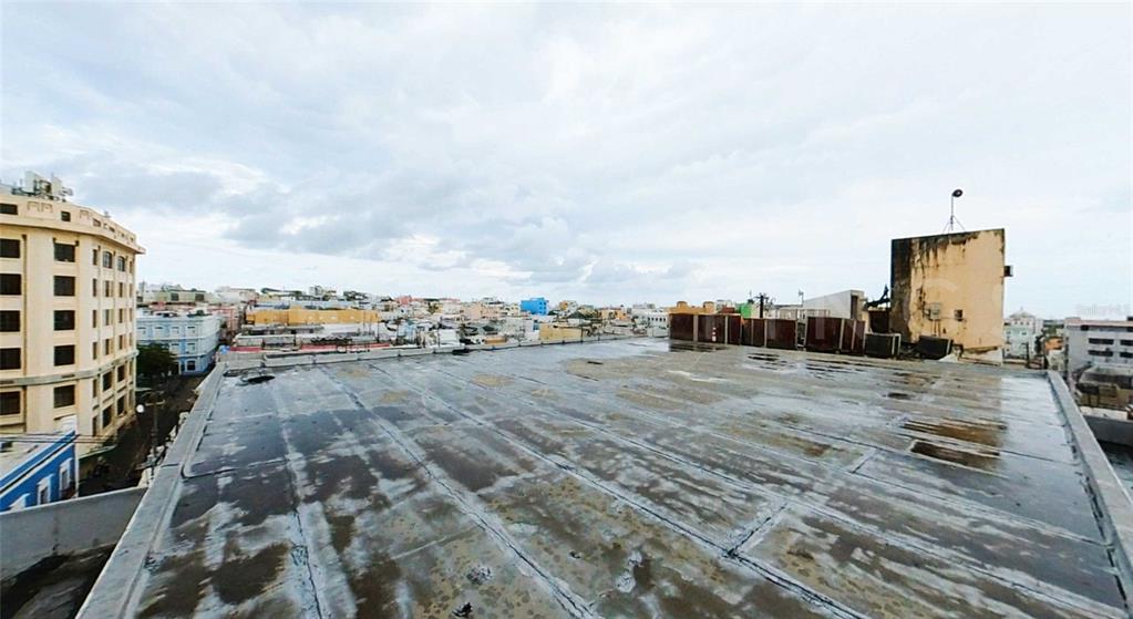 A flat, wet rooftop terrace overlooks a dense urban cityscape under a cloudy sky — 201 TETUAN STREET, SAN JUAN, PR