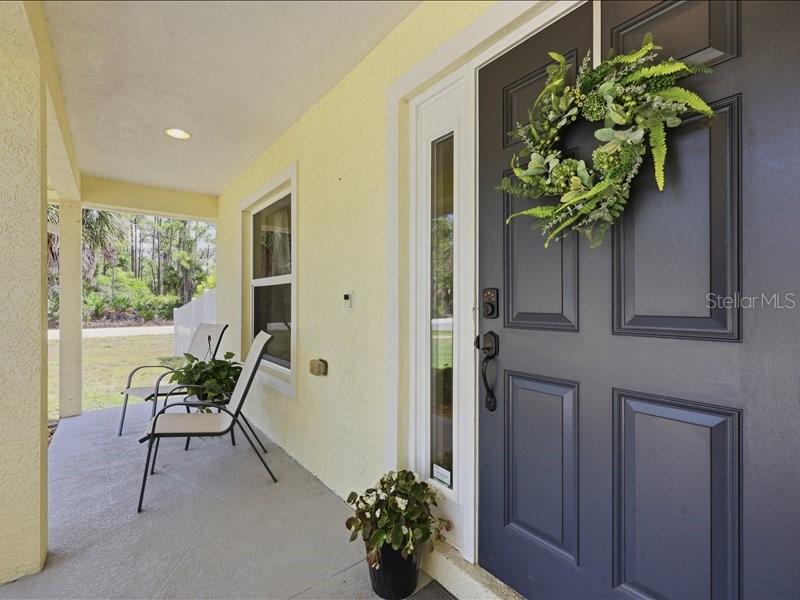 A covered porch features a dark front door with a wreath and two patio chairs — 1006 RHINELANDER STREET, PORT CHARLOTTE, FL