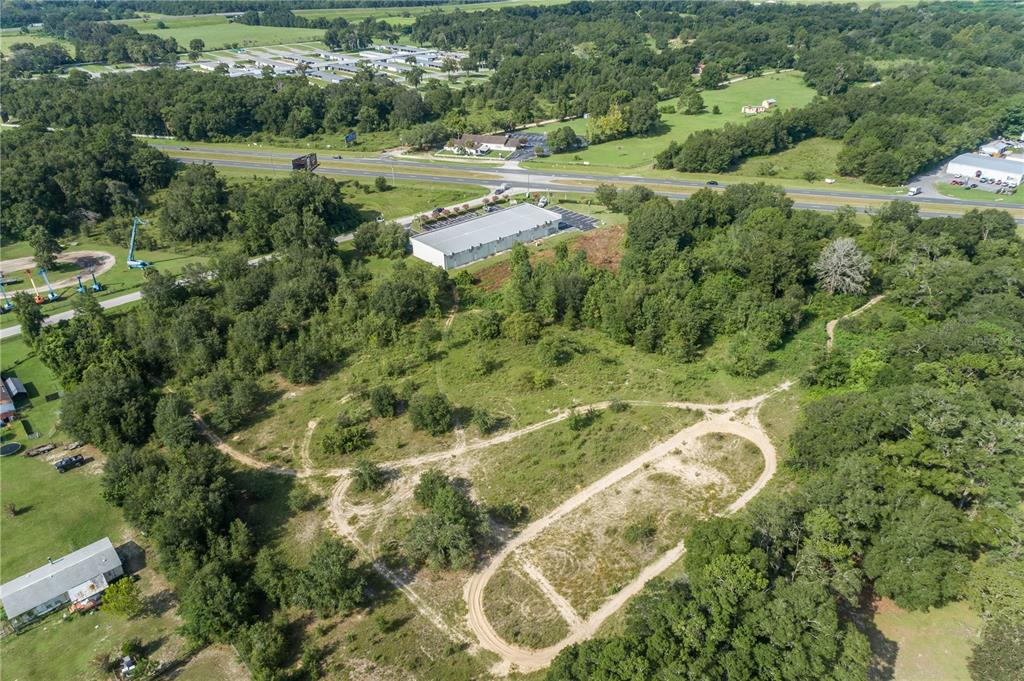 An aerial view shows a large, undeveloped grassy lot with dirt paths near a highway — 7711 SE 126TH PLACE, BELLEVIEW, FL