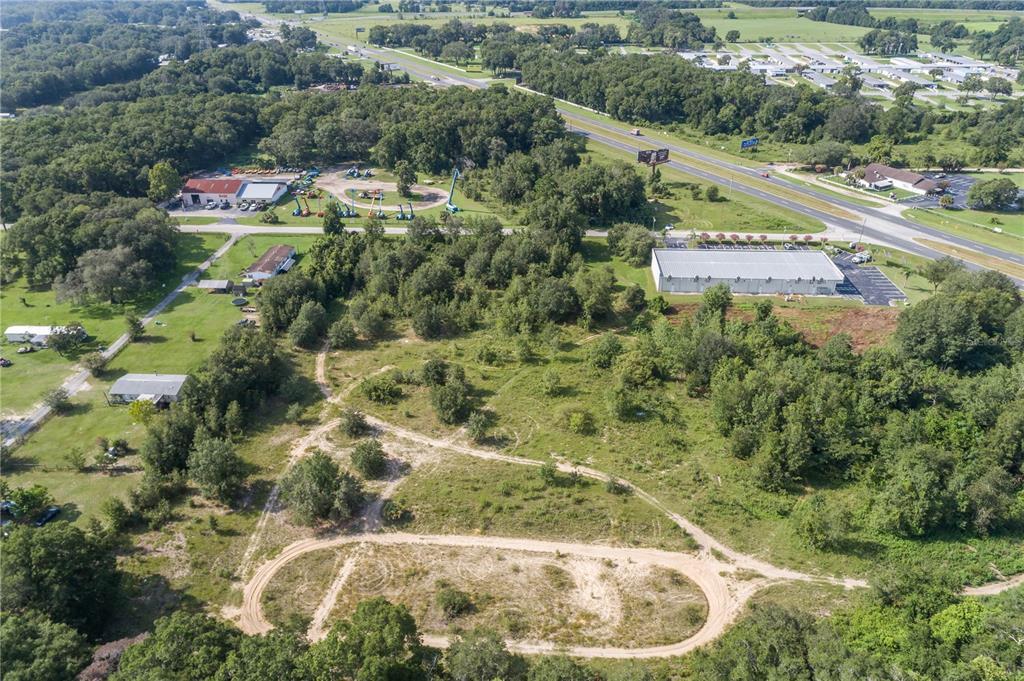 An aerial view shows a large, undeveloped grassy lot with dirt paths near a highway — 7711 SE 126TH PLACE, BELLEVIEW, FL