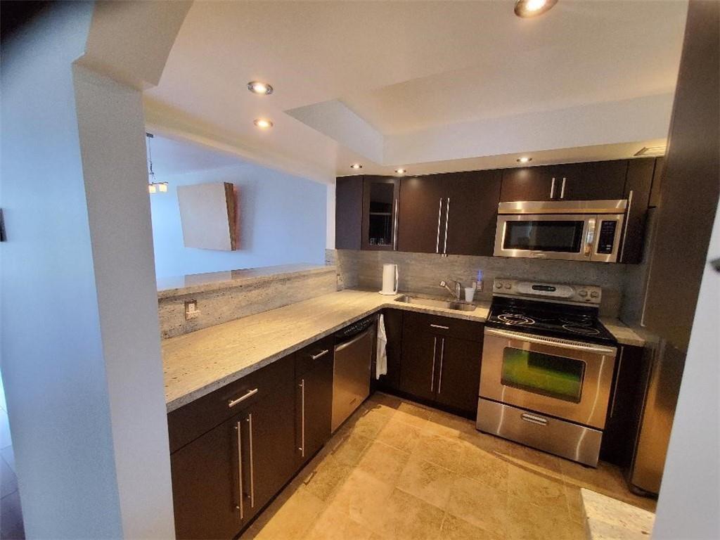 A kitchen features dark wood cabinets, stainless steel appliances, and light-colored granite countertops — 3000 S Course Drive # 505, Pompano Beach FL 33069, POMPANO BEACH, FL