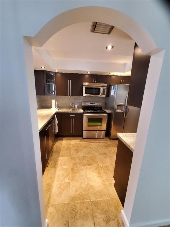 A kitchen with dark cabinets, stainless steel appliances, and tile flooring viewed through an archway — 3000 S Course Drive # 505, Pompano Beach FL 33069, POMPANO BEACH, FL