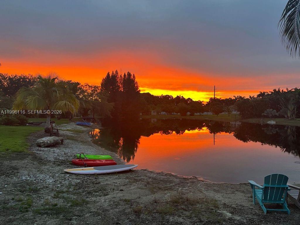 A vibrant sunset reflects over a calm lake with kayaks and a paddleboard on shore — 18901 SW 63rd St, Southwest Ranches FL 33332, SOUTHWEST RANCHES, FL