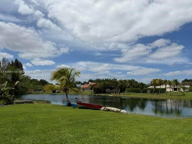 A red boat sits on the grassy bank of a pond with houses in the background — 18901 SW 63rd St, Southwest Ranches FL 33332, SOUTHWEST RANCHES, FL