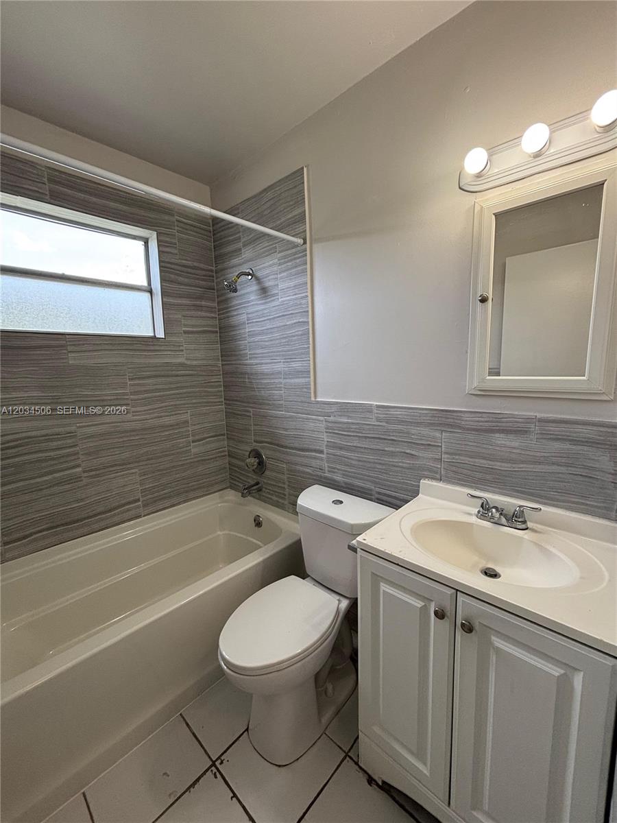 A bathroom features a white vanity, a toilet, and a tub with gray tiled walls — 14120 NW 24th Ct # 303, Opa-Locka FL 33054, OPA-LOCKA, FL