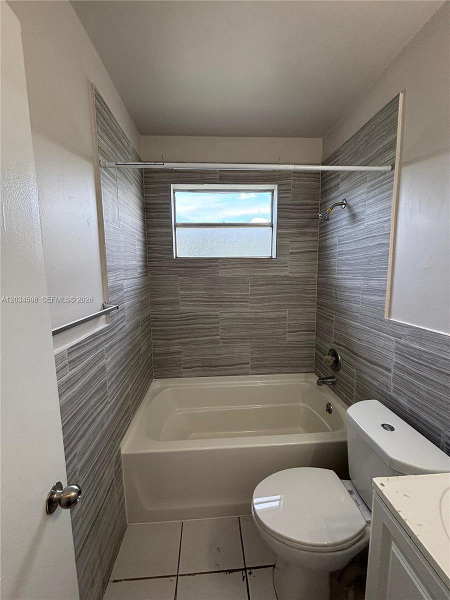 A bathroom features a white bathtub, a toilet, and walls tiled with gray horizontal patterns — 14120 NW 24th Ct # 303, Opa-Locka FL 33054, OPA-LOCKA, FL