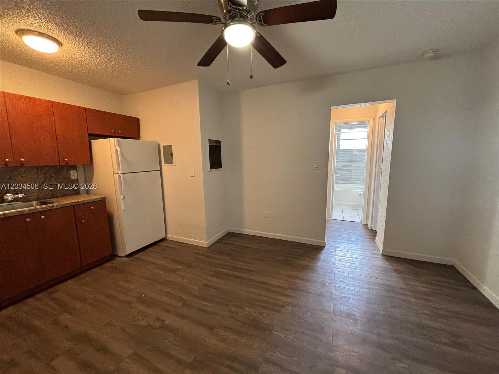 A kitchen with wood cabinets, a white refrigerator, and wood-look flooring leads to a bathroom — 14120 NW 24th Ct # 303, Opa-Locka FL 33054, OPA-LOCKA, FL