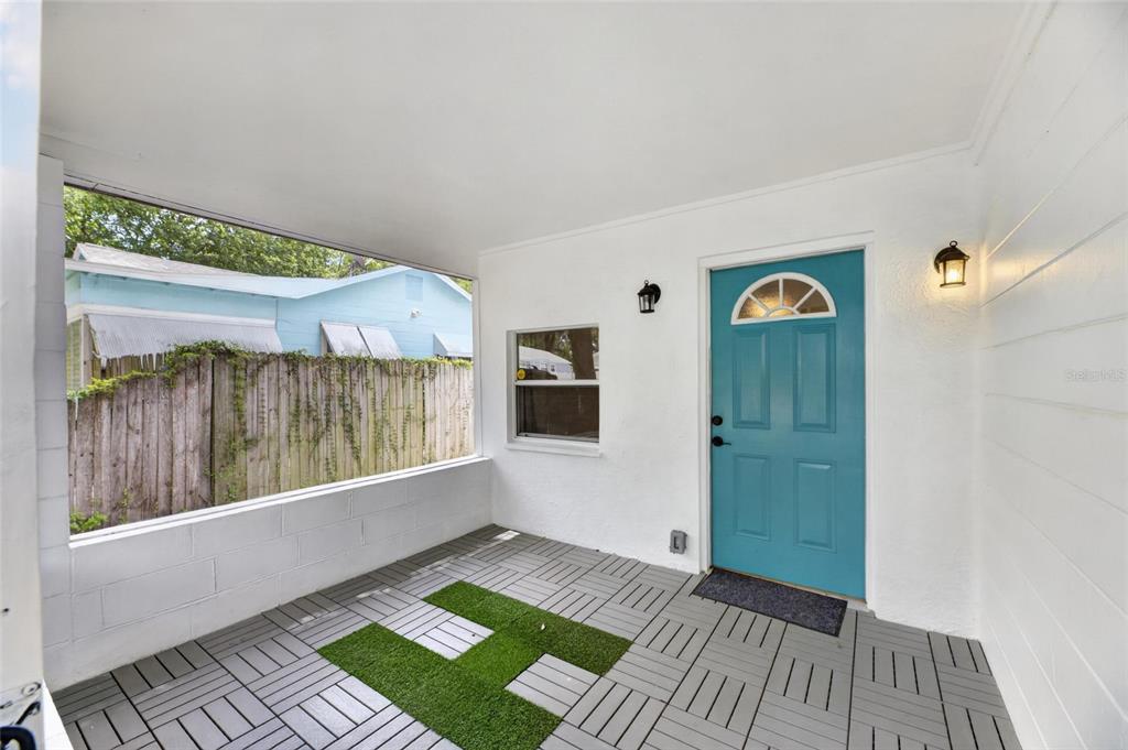 A covered porch features white walls, a teal front door, and gray interlocking floor tiles — 1005 E FLORA STREET, TAMPA, FL