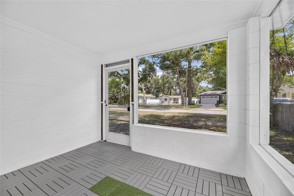 A screened-in porch features white block walls, gray interlocking floor tiles, and a glass door — 1005 E FLORA STREET, TAMPA, FL