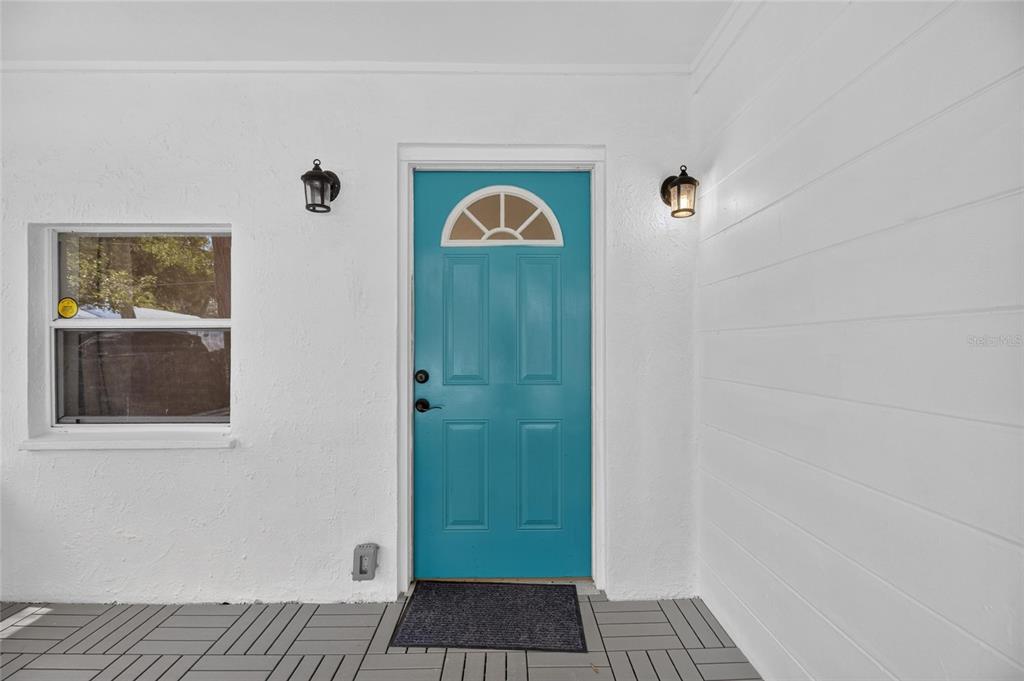 A bright teal front door is centered on a white exterior wall with two sconces — 1005 E FLORA STREET, TAMPA, FL