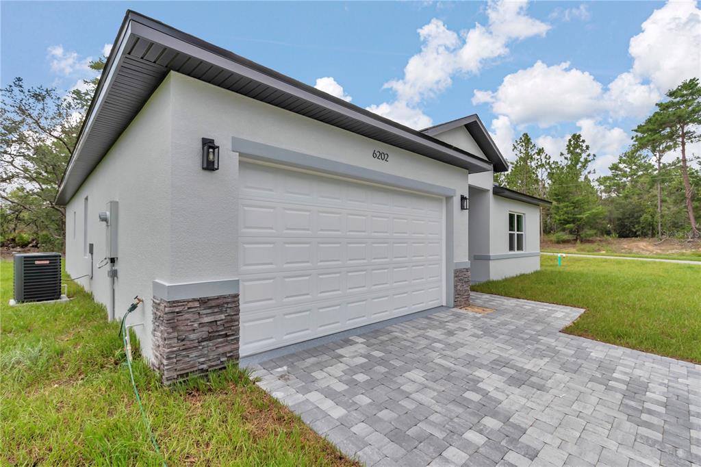A white stucco house exterior features a two-car garage, stone accents, and a paver driveway — 6202 N MARINER TERRACE, CITRUS SPRINGS, FL