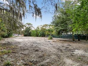 A cleared, sandy residential lot is surrounded by mature trees and a green privacy fence — 6935 TURQUOISE LANE, ORLANDO, FL