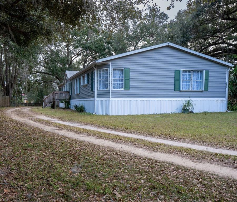 A gray manufactured home with white skirting sits on a lot with a dirt driveway — 13811 COUNTY ROAD 109D, LADY LAKE, FL