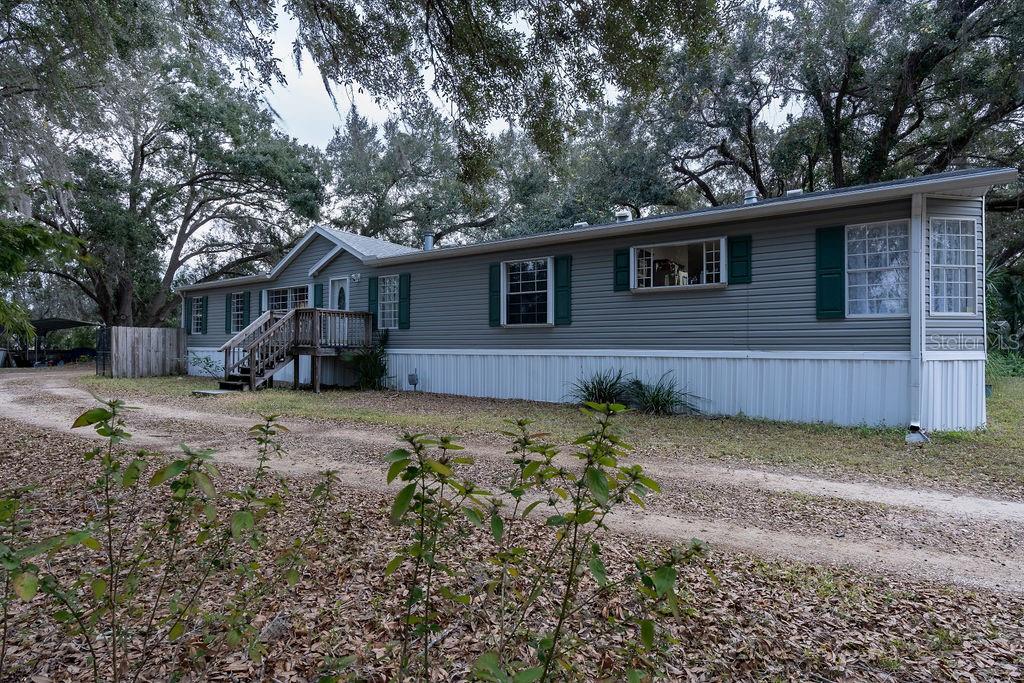 A single-story manufactured home with gray siding and green shutters sits on a dirt driveway — 13811 COUNTY ROAD 109D, LADY LAKE, FL
