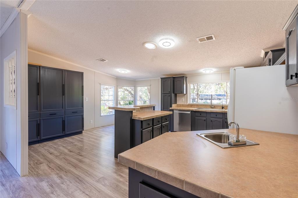 A kitchen with dark cabinets, tiled countertops, stainless steel appliances, and light wood-look flooring — 13811 COUNTY ROAD 109D, LADY LAKE, FL