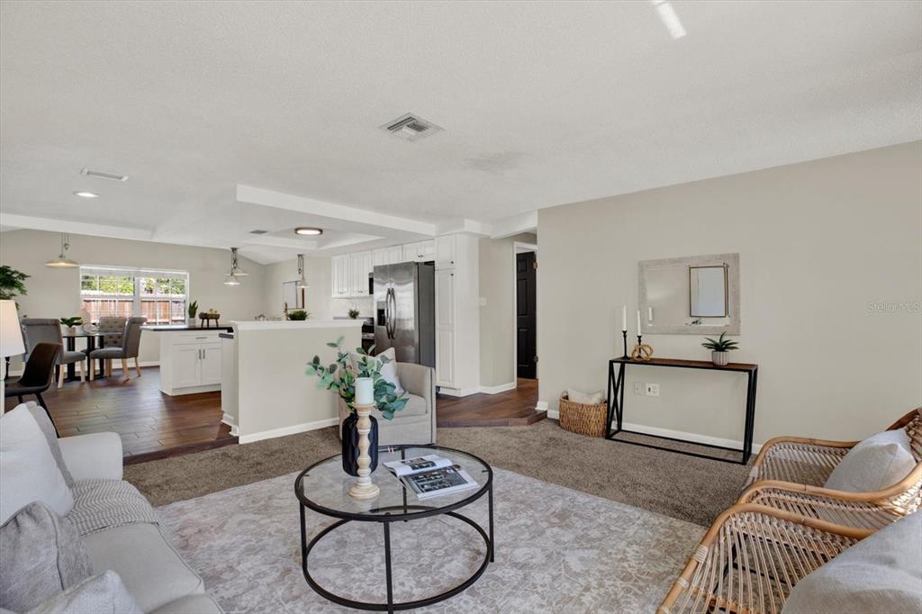 A living room with carpeted flooring opens to a kitchen featuring white cabinets and island — 10898 119TH STREET N, SEMINOLE, FL