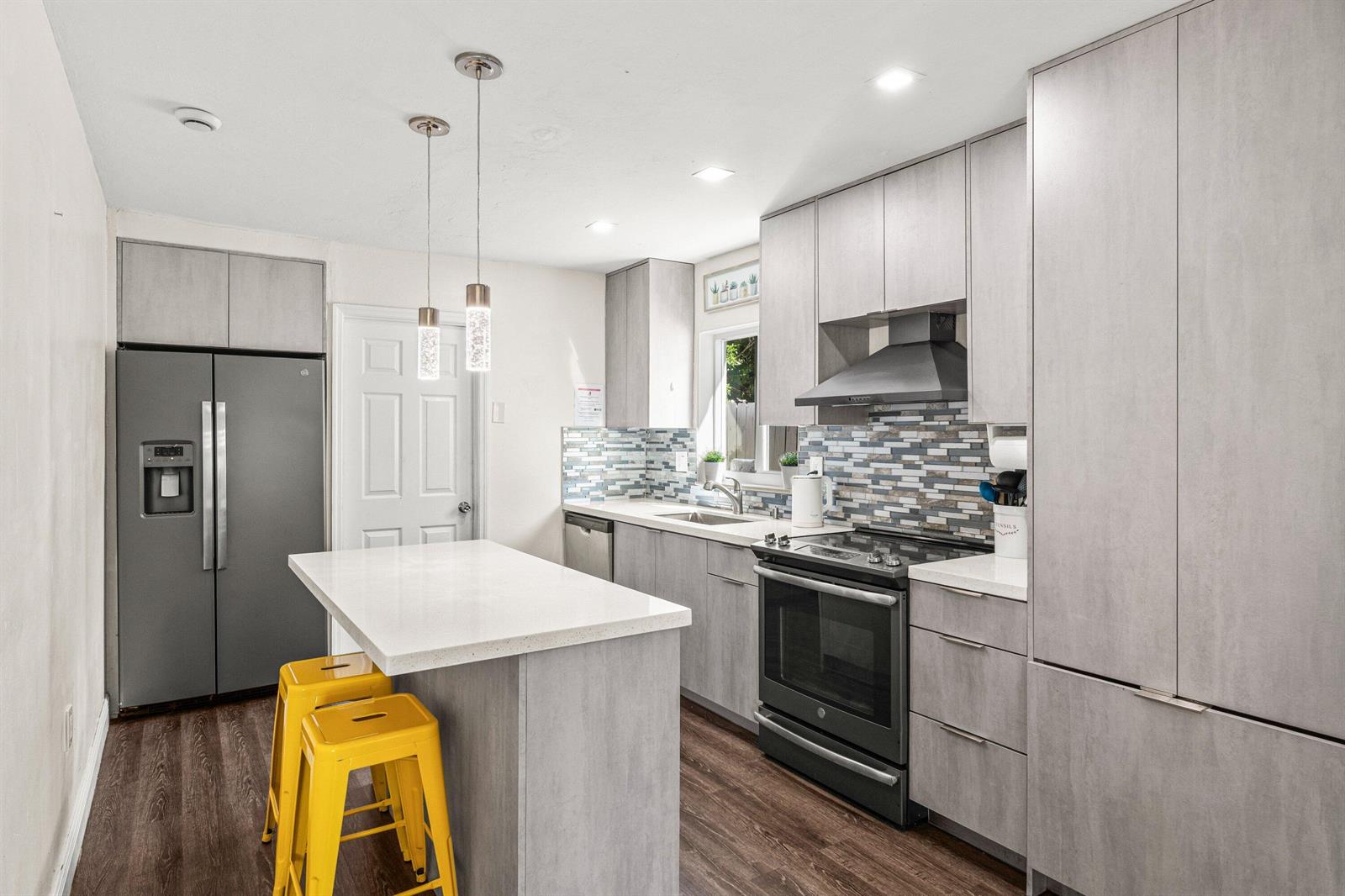 A kitchen features gray cabinetry, a white island with yellow stools, and a tiled backsplash — 1121 N 66th Terrace, Hollywood FL 33024, HOLLYWOOD, FL