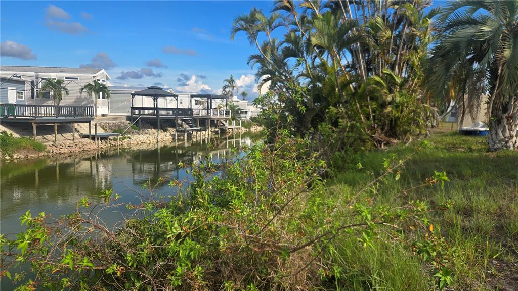 A canal runs alongside a grassy bank with palm trees and elevated mobile homes nearby — 1399 FLAMINGO DRIVE, ENGLEWOOD, FL
