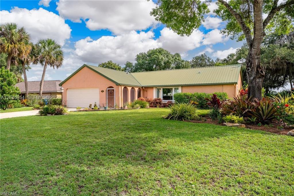 A single-story peach-colored house with a green metal roof and arched entryway — 4559 Springview Cir, La Belle FL 33935, LA BELLE, FL