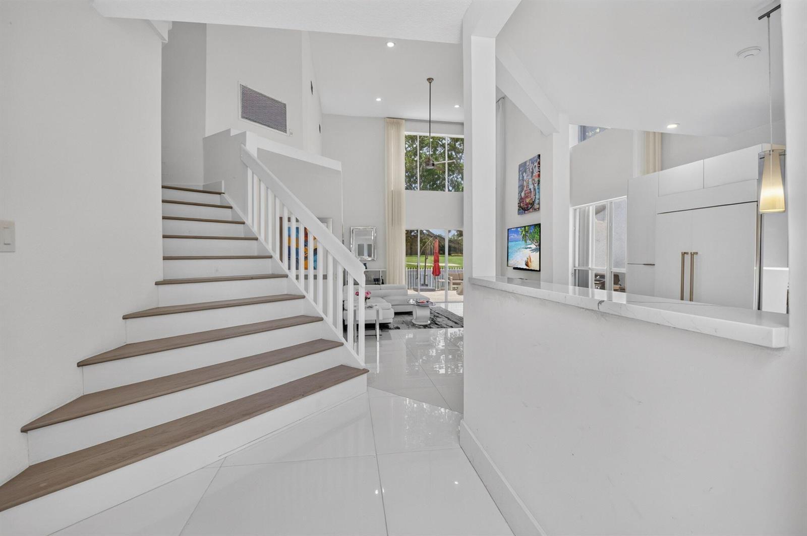 A bright, modern entryway features white tile floors, a wooden staircase, and a high ceiling — 5835 NW 42nd Terrace, Boca Raton FL 33496, BOCA RATON, FL