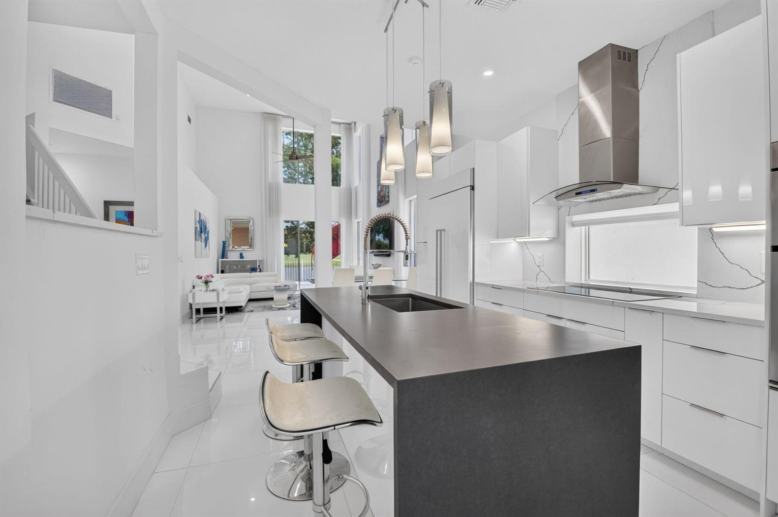 A modern kitchen with a dark island, white cabinetry, and a view of the living area — 5835 NW 42nd Terrace, Boca Raton FL 33496, BOCA RATON, FL