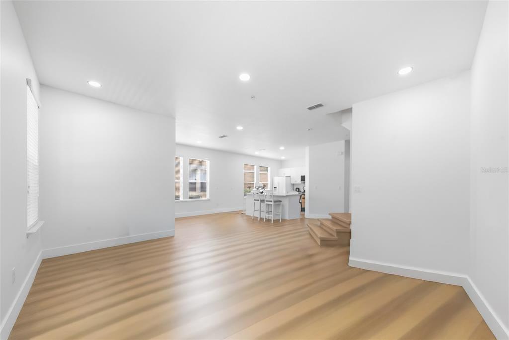 An empty room with light wood-look flooring, white walls, recessed lighting, and a wooden staircase — 10359 LAKE DISTRICT LANE UNIT 58B, ORLANDO, FL