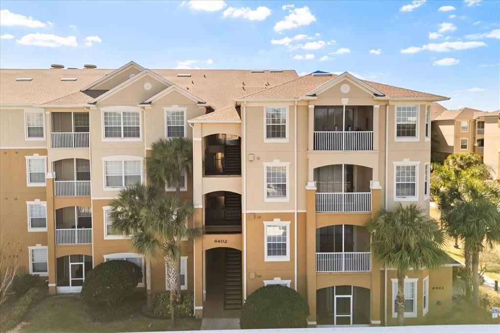 An exterior view of a multi-story apartment building with tan stucco walls and balconies — 6402 CAVA ALTA DRIVE UNIT 206, ORLANDO, FL