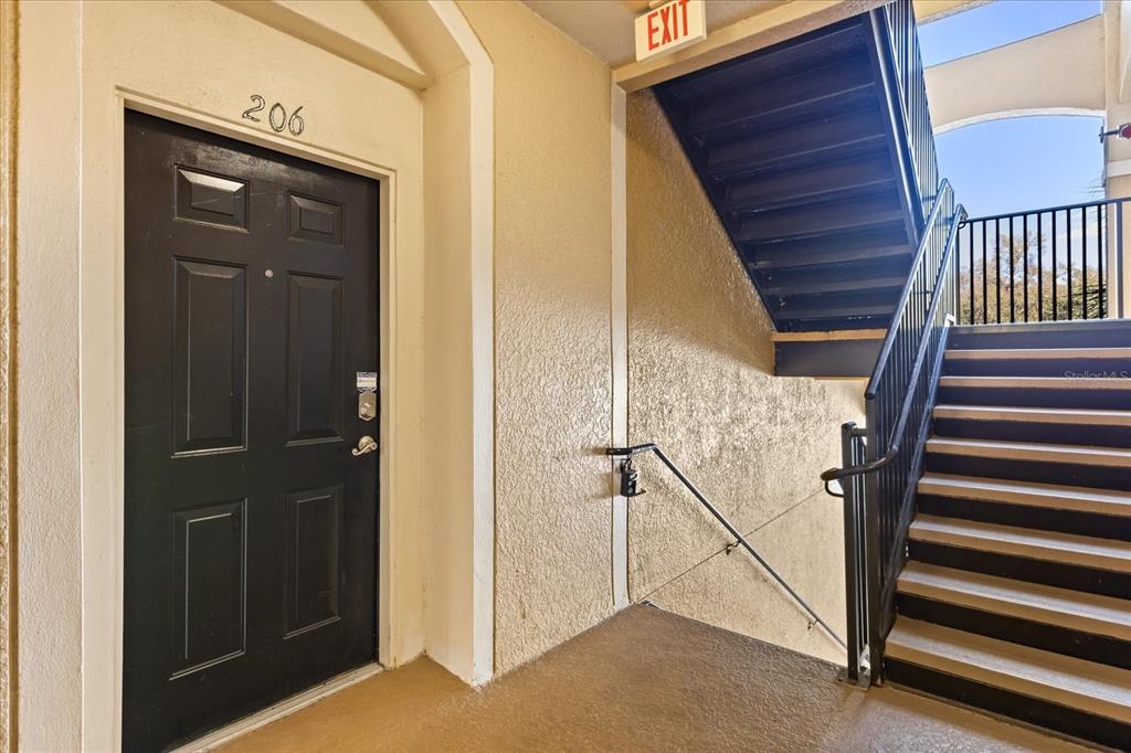 A black apartment door labeled 206 is next to an outdoor staircase with metal railings — 6402 CAVA ALTA DRIVE UNIT 206, ORLANDO, FL