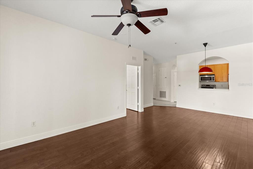 An empty living room features dark wood flooring, a ceiling fan, and an arched kitchen opening — 6402 CAVA ALTA DRIVE UNIT 206, ORLANDO, FL