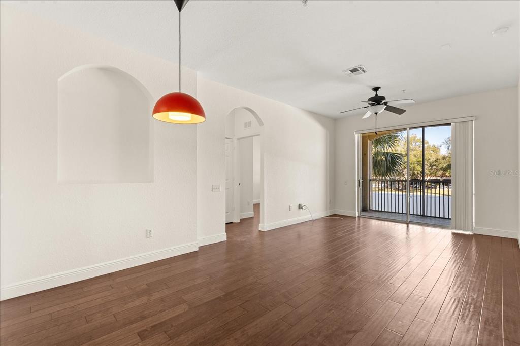 An empty living room features dark wood flooring, a red pendant light, and a balcony — 6402 CAVA ALTA DRIVE UNIT 206, ORLANDO, FL