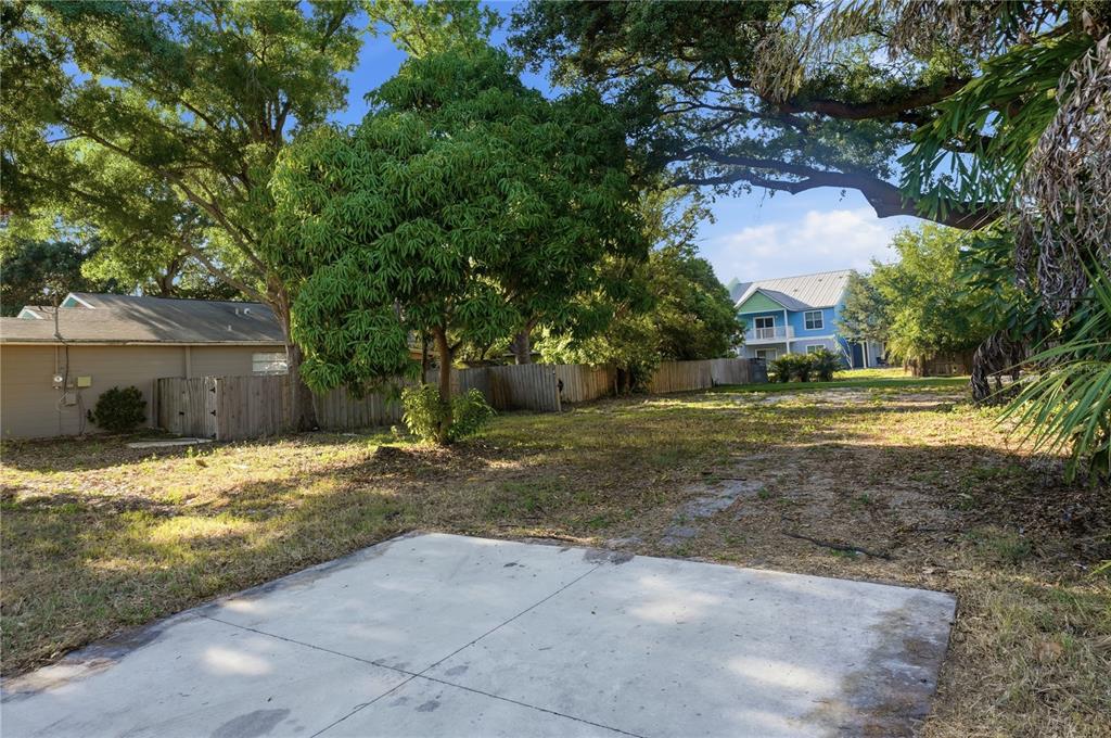 A concrete pad sits in the foreground of a grassy, tree-filled backyard with wooden fencing — 2929 W AVERILL AVENUE, TAMPA, FL