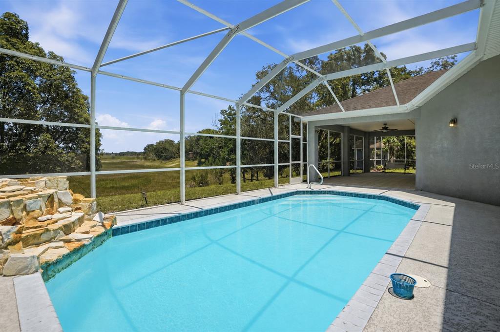 A screened-in swimming pool with a rock waterfall feature overlooks a grassy field — 9011 FOXDALE LANE, SPRING HILL, FL